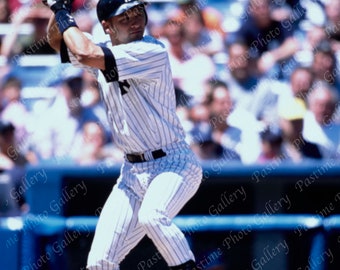 Puede incluir: Un jugador de béisbol con un uniforme a rayas blancas y azules balancea un bate. El jugador lleva un casco negro y tacos negros. El jugador está en un estadio de béisbol con una multitud de personas en el fondo.