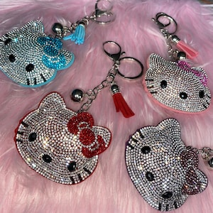 May include: Five Hello Kitty keyrings with rhinestone embellishments. Each keyring features a different coloured bow and tassel.