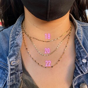 May include: Three gold chain necklaces layered on a person's neck. The chains are labeled with the lengths 18, 20, and 22 inches.