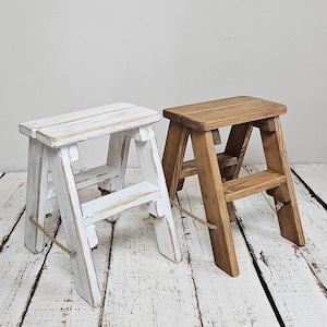 Peut inclure: Deux tabourets d'escalier en bois, l'un peint en blanc et l'autre en bois naturel. Les deux ont une poignée en corde et sont faits de bois rustique.