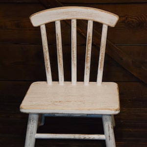 May include: A white wooden chair with a distressed finish. The chair has a simple design with a curved back and straight legs.