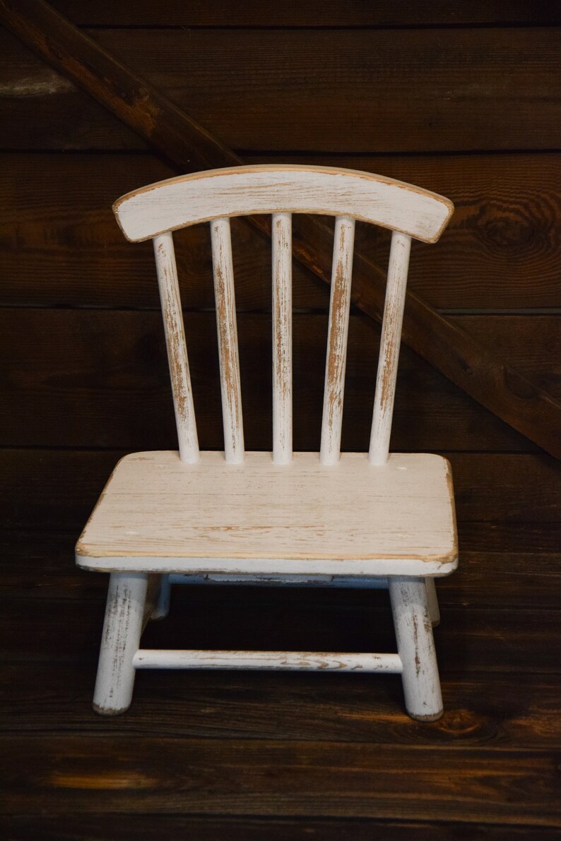May include: A white wooden chair with a distressed finish. The chair has a simple design with a curved back and straight legs.