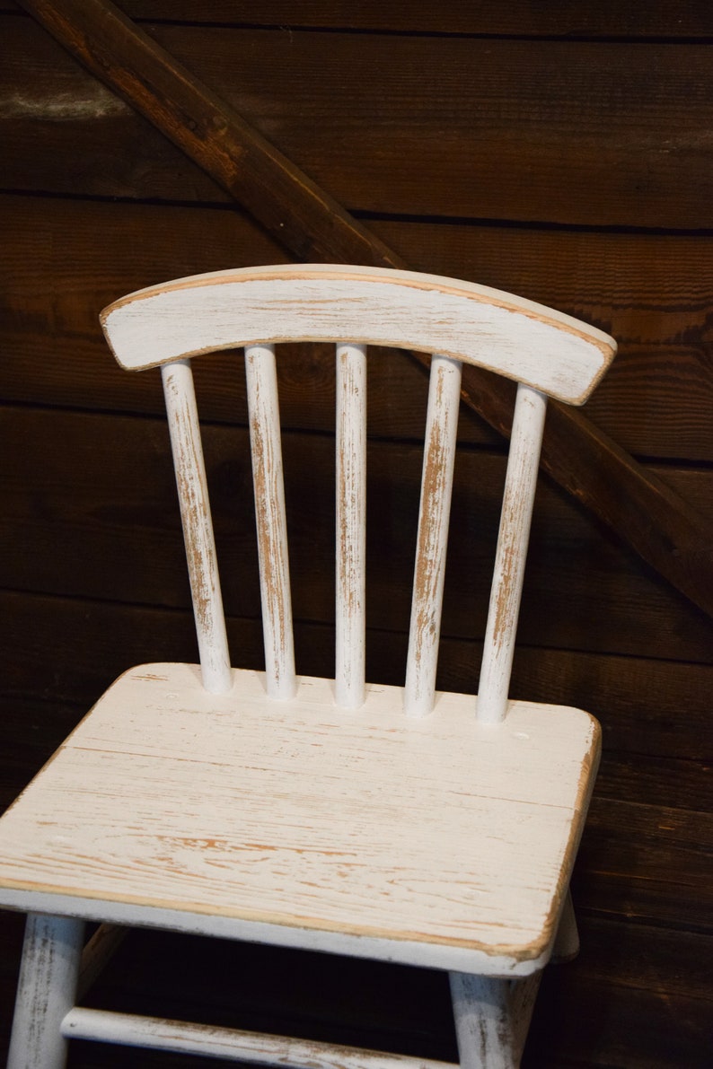 May include: White wooden chair with a distressed finish. The chair has a curved back and a slatted design.