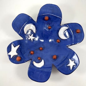 May include: A blue ceramic flower-shaped dish with white crescent moons and stars, and brown dots.