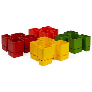 Może przedstawiać: Trzy modułowe doniczki w kolorze czerwonym, żółtym i zielonym. Doniczki mają kształt puzzli i można je układać w różnych konfiguracjach.