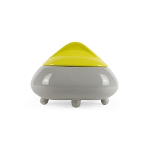 May include: A gray ceramic trinket box with a yellow lid and three small feet. The lid has a rounded, triangular shape.