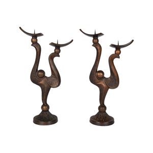 Puede incluir: Un par de candelabros de bronce con un diseño único y abstracto. Cada candelabro presenta una base curva y estilizada y tres portavelas.