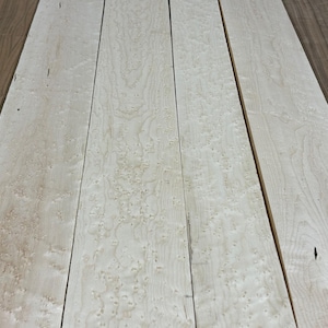 May include: Close-up of several light-colored wooden planks with a speckled pattern. The planks are arranged side by side, showcasing the natural grain and texture of the wood. The wood has a light, creamy color with darker accents.