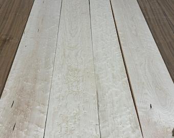 May include: Close-up of several light-colored wooden planks with a speckled pattern. The planks are arranged side by side, showcasing the natural grain and texture of the wood. The wood has a light, creamy color with darker accents.