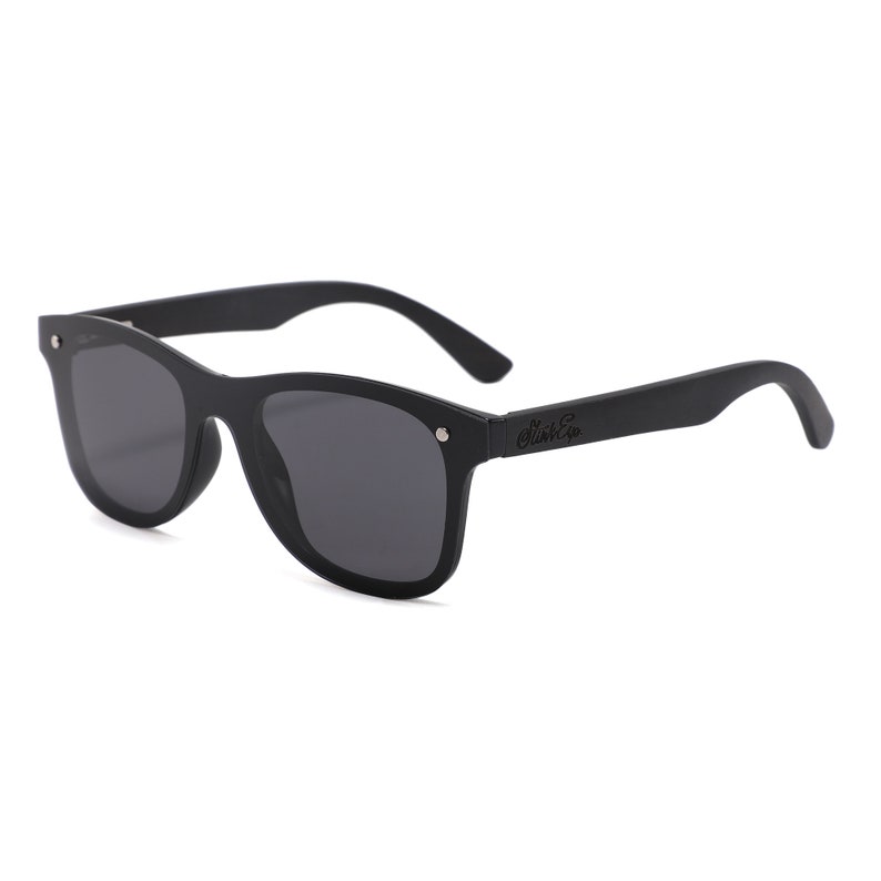 May include: Black sunglasses with dark gray lenses. The sunglasses have a rectangular frame and curved arms. The brand name "Stink Co" is printed on the right arm. The sunglasses are designed for eye protection from the sun.