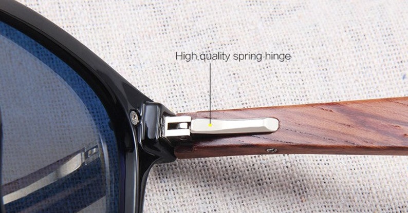 May include: Close-up of sunglasses with a black frame and blue lenses. The wooden arm features a high-quality spring hinge. The text "High quality spring hinge" is visible.