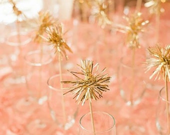 May include: Gold glitter starburst toppers in clear glass champagne flutes on a peach-colored tablecloth.