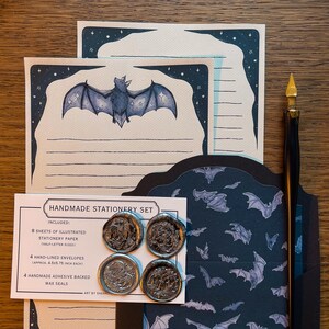 May include: A handmade stationery set featuring illustrated stationery paper, hand-lined envelopes, and adhesive-backed wax seals. The stationery paper has a bat illustration with a starry border. The set includes 8 sheets of paper, 4 envelopes (approx. 4.5x5.75 inch each), and 4 wax seals.