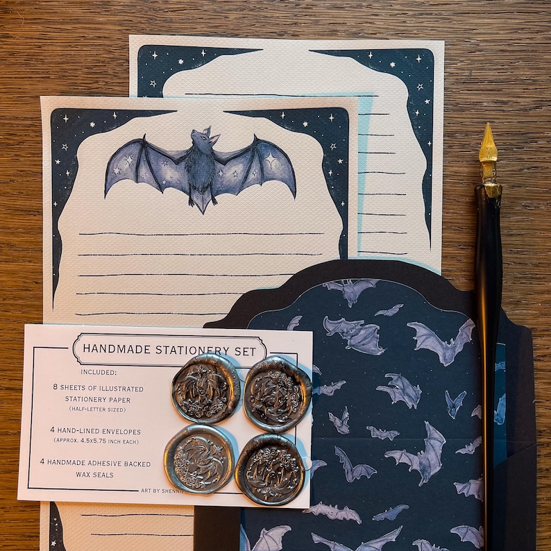 May include: A handmade stationery set featuring illustrated stationery paper, hand-lined envelopes, and adhesive-backed wax seals. The stationery paper has a bat illustration with a starry border. The set includes 8 sheets of paper, 4 envelopes (approx. 4.5x5.75 inch each), and 4 wax seals.