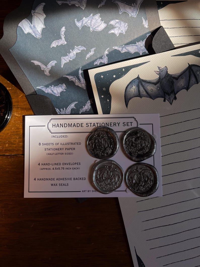 May include: Handmade stationery set featuring illustrated paper and envelopes with bat designs. Includes four adhesive-backed wax seals. The set includes 8 sheets of half-letter sized paper and 4 envelopes, each approximately 4.5 x 5.75 inches. The text on the card reads "HANDMADE STATIONERY SET".