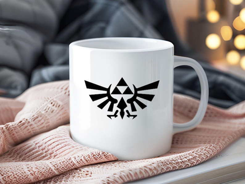 May include: White ceramic mug with a black emblem of a triangle above a stylized bird with wings. The mug has a curved handle and is set against a soft, textured background. The background is a soft pink.