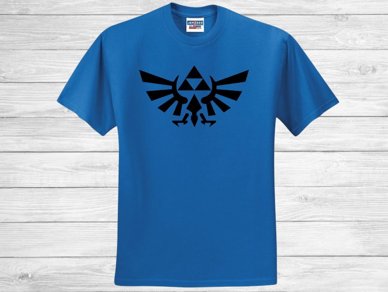 May include: A royal blue t-shirt with a black emblem design. The emblem is a stylized symbol with a central triangle and wing-like shapes. The t-shirt has a crew neck and short sleeves.