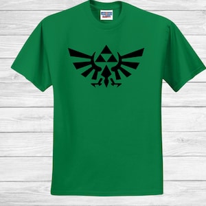 May include: A green t-shirt with a black emblem design. The emblem is a symmetrical shape with a triangle and wing-like elements. The shirt is made of a soft material. The design is centered on the shirt.