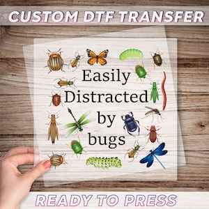 May include: A clear, rectangular DTF transfer sheet with the text "CUSTOM DTF TRANSFER" and "READY TO PRESS". The sheet features various colorful bug illustrations and the phrase "Easily Distracted by bugs".