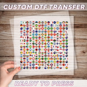 May include: A transparent sheet printed with numerous circular flag designs, labelled "CUSTOM DTF TRANSFER" and "READY TO PRESS". The flags represent different countries. The sheet is held by a hand.