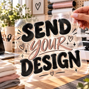 May include: A clear transfer sheet featuring the text SEND YOUR DESIGN in a bold, rounded font. The words SEND and DESIGN are in black, while the word YOUR is in a soft pink. The design includes small heart and star accents.