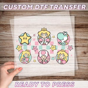 May include: A sheet of clear transfer paper with a pink and blue design featuring characters from the Super Mario Bros. video game series. The characters include Princess Peach, Toad, and Yoshi. The design also includes stars and a checkered pattern. The text "CUSTOM DTF TRANSFER" appears at the top of the sheet and "READY TO PRESS" appears at the bottom.