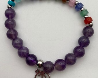 May include: A beaded bracelet featuring large, round, purple amethyst stones and smaller, colorful rectangular beads. A silver charm with a Sagittarius symbol hangs from the bracelet. The bracelet is strung on a stretchy cord.