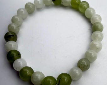 May include: A beaded bracelet composed of round, polished beads in shades of white and green. The bracelet features a mix of solid green and off-white beads, strung together to form a complete circle. The beads are approximately 0.3 inches in diameter.