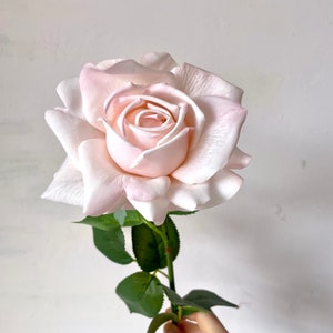 May include: A single, pale pink artificial rose with green leaves and a stem.