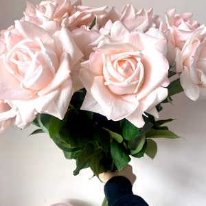 May include: A bouquet of blush pink artificial roses with green leaves.