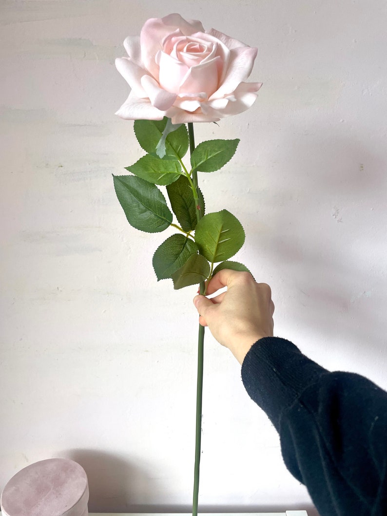 May include: A single, long-stemmed artificial rose with a light pink bloom and green leaves.