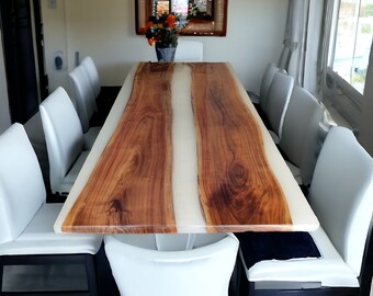 May include: A long wooden dining table with a white resin inlay. The table is surrounded by white chairs with black legs.