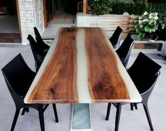 May include: A long, rectangular dining table made of dark wood with a white epoxy river running down the center. The table is surrounded by six black chairs.