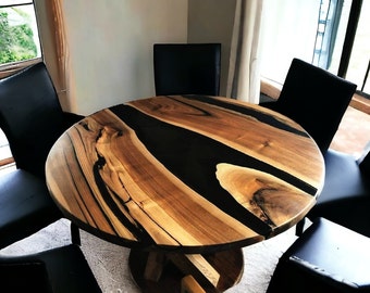 May include: Round wooden dining table with a black epoxy resin inlay. The table has a natural wood grain pattern and is surrounded by black chairs.