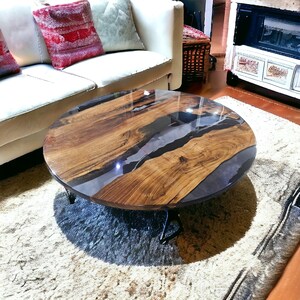 May include: A round wooden coffee table with a dark gray epoxy resin inlay. The table has a natural wood finish and is supported by a black metal base.