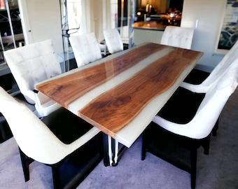 May include: A long, rectangular dining table with a white epoxy resin top and a natural wood inlay. The table is surrounded by white chairs with black legs.