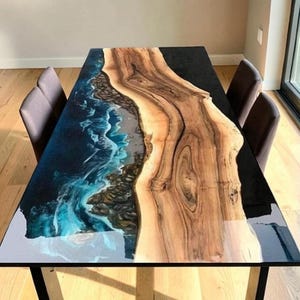May include: A rectangular dining table featuring a live edge wood slab centerpiece with prominent grain patterns, flanked by sections of dark black resin and a detailed blue and white ocean wave design with sandy textures along the wood edge.