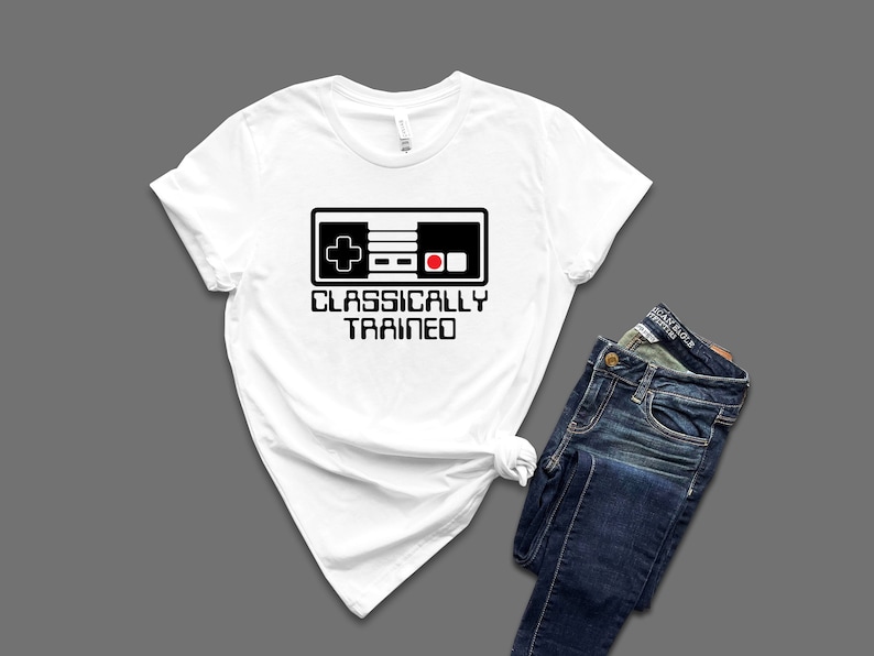 May include: White t-shirt with a black and white illustration of a classic video game controller and the text "Classically Trained".