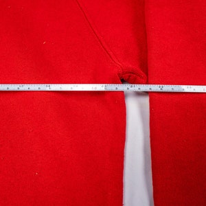 May include: A close-up of a red sweatshirt with a measuring tape across the chest. The tape measures 16 inches.
