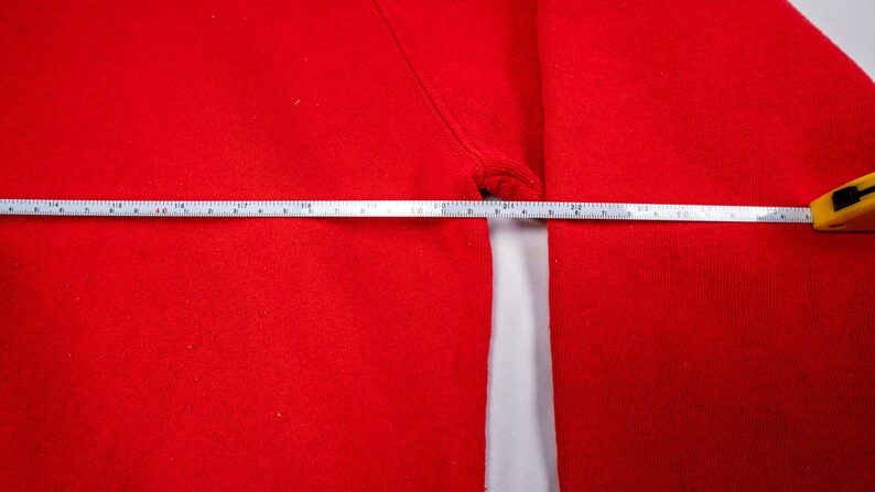 May include: A close-up of a red sweatshirt with a measuring tape across the chest. The tape measures 16 inches.