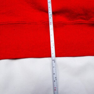May include: A red sweatshirt with a ribbed hem. A white measuring tape is placed next to the hem, showing a measurement of 28 inches.