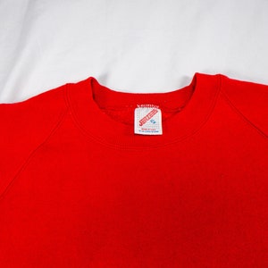 May include: Red sweatshirt with a white tag that says "JERZEES" in red letters.