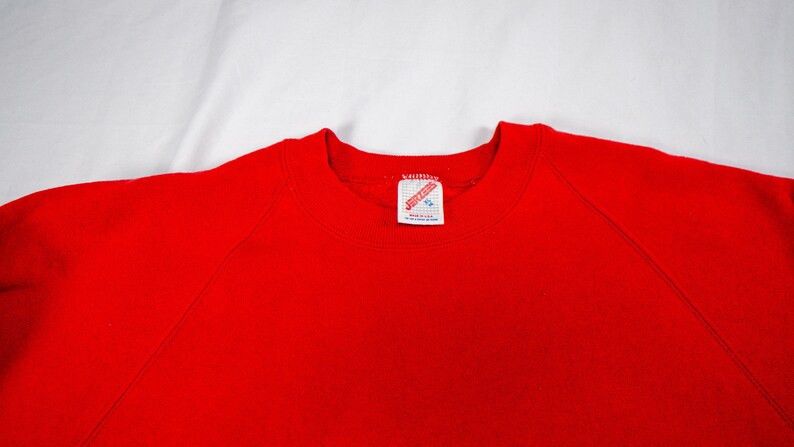 May include: Red sweatshirt with a white tag that says "JERZEES" in red letters.