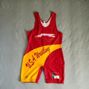 May include: Red and yellow wrestling singlet with a North Carolina state outline and the text "USA Wrestling" on the side. The singlet also features a small North Carolina state flag on the back.