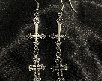 May include: A pair of silver dangle earrings with a detailed cross design. Each earring features two crosses, one smaller than the other, connected by a chain.