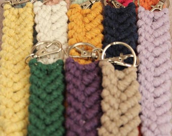May include: A collection of 10 colorful macrame keychains with silver key rings. The keychains are made with a variety of colors, including yellow, white, orange, blue, green, purple, and pink.