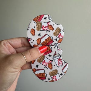 Könnte beinhalten: Zwei runde Auto-Untersetzer mit weißem Hintergrund und einem sich wiederholenden Muster aus Brathähnchen, Waffelpommes und einem Getränkebecher. Die Untersetzer haben einen Ausschnitt zum einfachen Herausnehmen aus einem Auto-Getränkehalter.