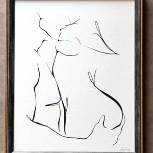 May include: A framed black and white line art drawing on textured paper depicting the abstract silhouettes of two figures in an embrace. The artwork features fluid, continuous black ink lines against a white background, enclosed in a dark frame.