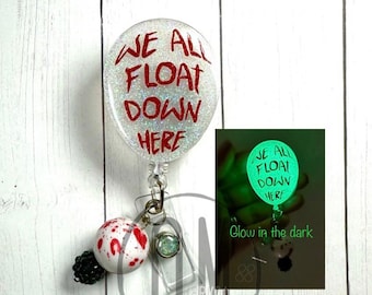 May include: A white and silver glitter badge reel with a red "We All Float Down Here" balloon charm. The charm glows green in the dark. The reel also has a black bead charm with red splatter paint and a clear crystal charm.