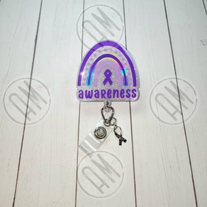 May include: Purple and white glitter rainbow with a purple ribbon and the word "awareness" on a white background. The rainbow is attached to a retractable badge holder with a clear plastic strap and a silver clip.